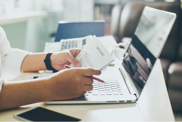 A person holding a resume, a laptop in front of them