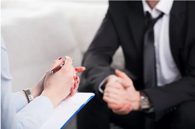 A woman with a clipboard and a man in a suit, talking to each other